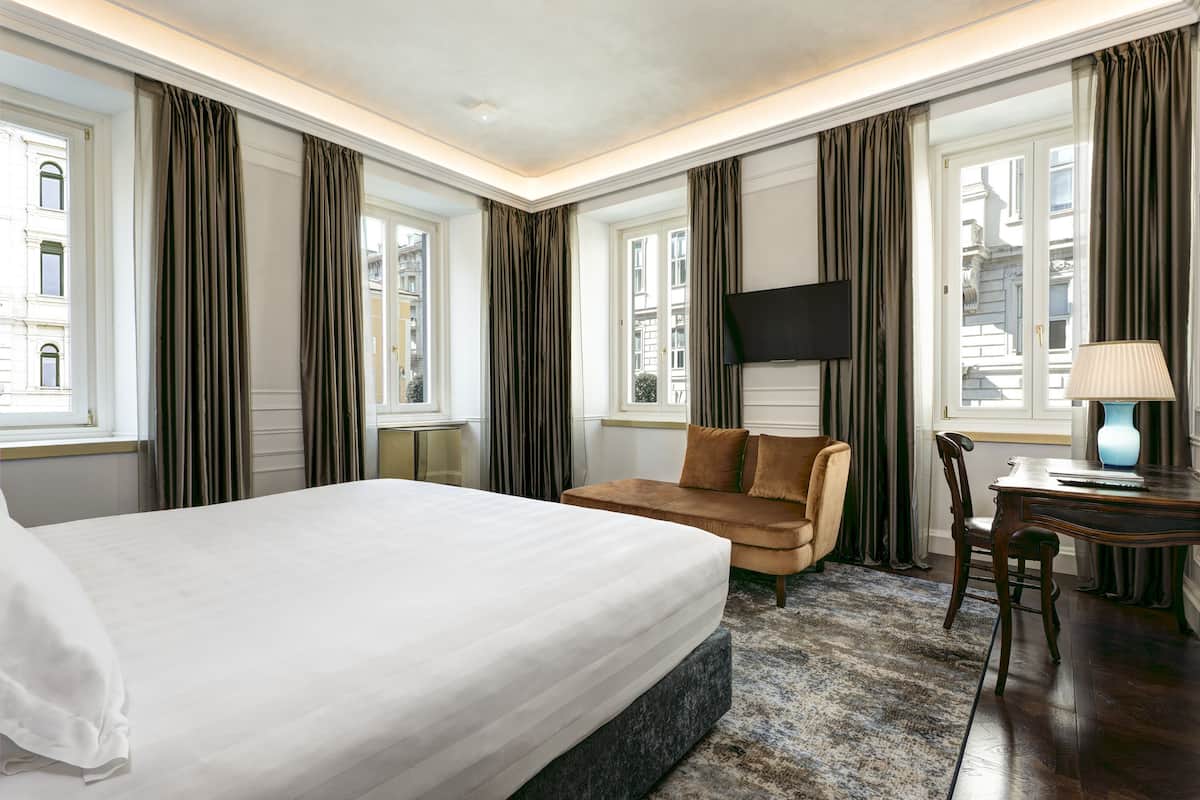 Habitación de hotel con una cama grande, un sofá, un escritorio con lámpara y un televisor instalado en la pared.