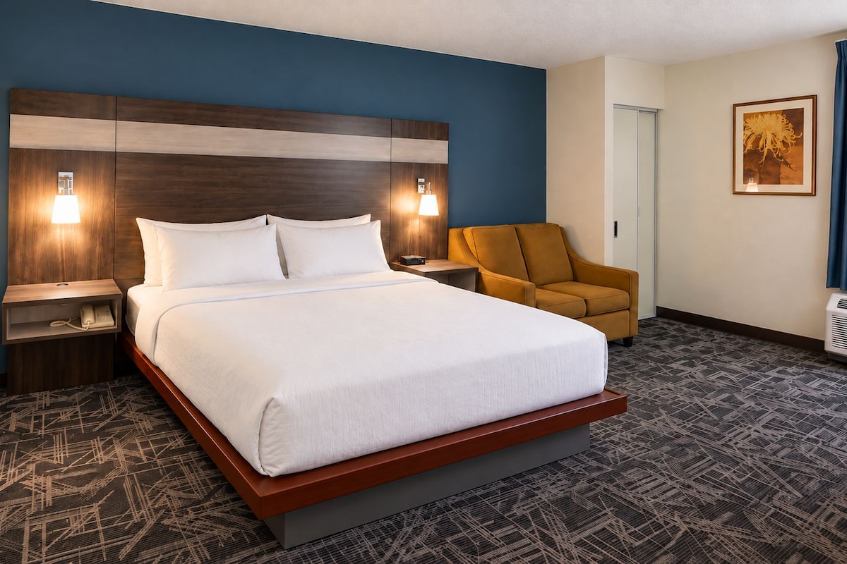Une chambre d’hôtel avec un grand lit, deux tables de chevet avec des lampes, une chaise et un radiateur fixé au mur.