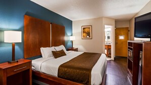 A hotel room with a large bed, wooden headboard, two bedside tables with lamps, a flat-screen TV, and a bathroom visible through an open door. - Best Western Plus Richmond Airport Hotel (Sandston)