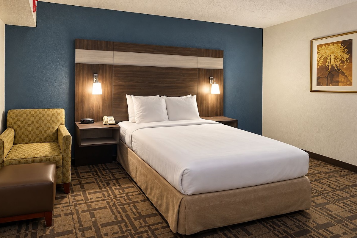 Une chambre d’hôtel avec un lit, une chaise, une table de chevet et une lampe fixée au mur.