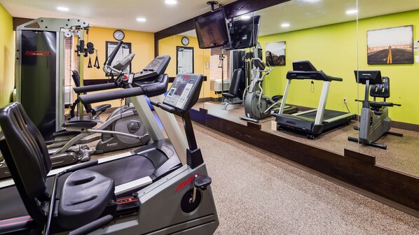 Ein Fitnessstudio mit verschiedenen Trainingsgeräten, einer Uhr und einem motivierenden Poster an der Wand.