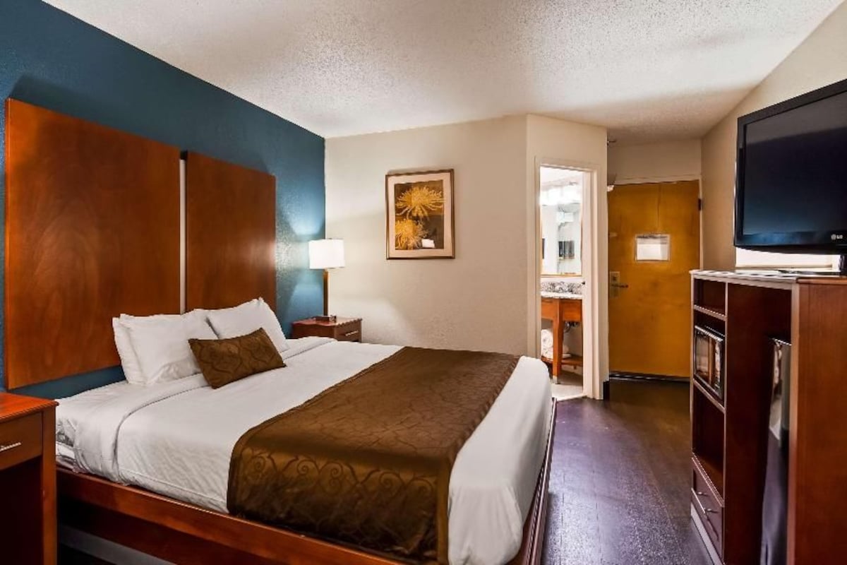 Une chambre d’hôtel avec un grand lit, des tables de chevet, une télévision et une armoire.