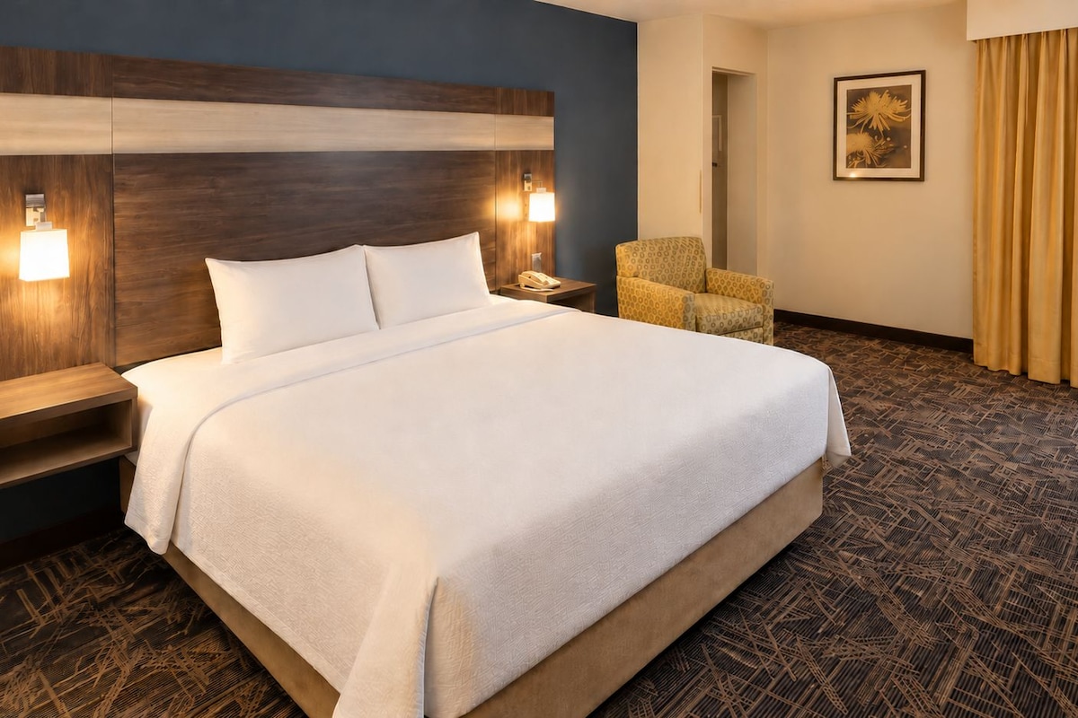 Une chambre d’hôtel avec un grand lit, des tables de chevet, une chaise et un tableau au mur.
