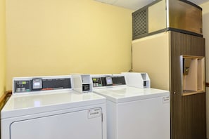 Une buanderie équipée de deux lave-linge à chargement frontal et d’un sèche-linge, tous dotés de panneaux de commande numériques.