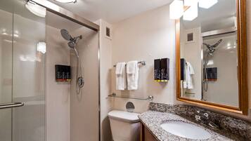 Un baño moderno con cabina de ducha de vidrio, inodoro, lavamanos con encimera de granito y un espejo grande.