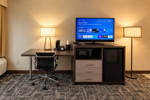 Een hotelkamer met een bureau, een stoel, een televisie waarop DIRECTV-zenders te zien zijn, een koffiezetapparaat, een magnetron en een koelkast.