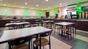 Une cafétéria avec des tables et des chaises, un distributeur de café et une horloge au mur.