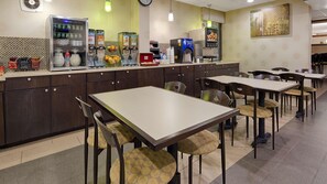 Une cafétéria équipée de distributeurs automatiques de boissons, d’une machine à café et d’un assortiment de produits alimentaires présentés sur le comptoir. Plusieurs tables et chaises sont disposées pour permettre aux clients de prendre leurs repas.