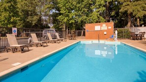 Une piscine avec des chaises longues et un espace délimité par une clôture, le tout entouré d’arbres.