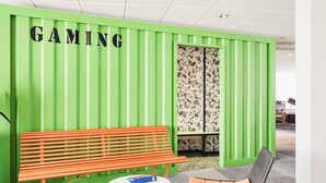 Un espacio de juegos con una pared verde, un banco de madera, una mesa redonda y dos sillas.