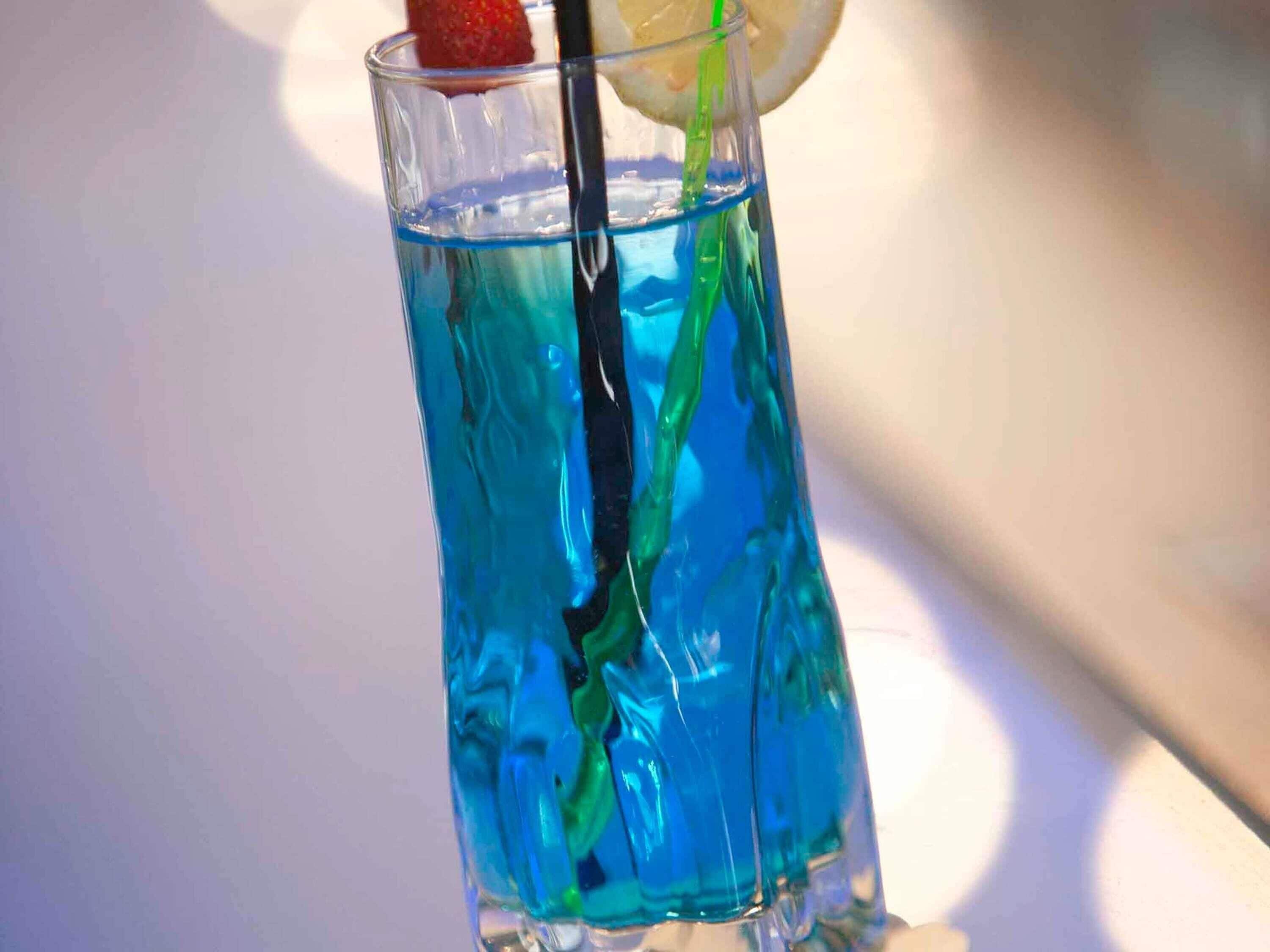 Un grand verre contenant un liquide bleu, une paille et une tranche de citron.
