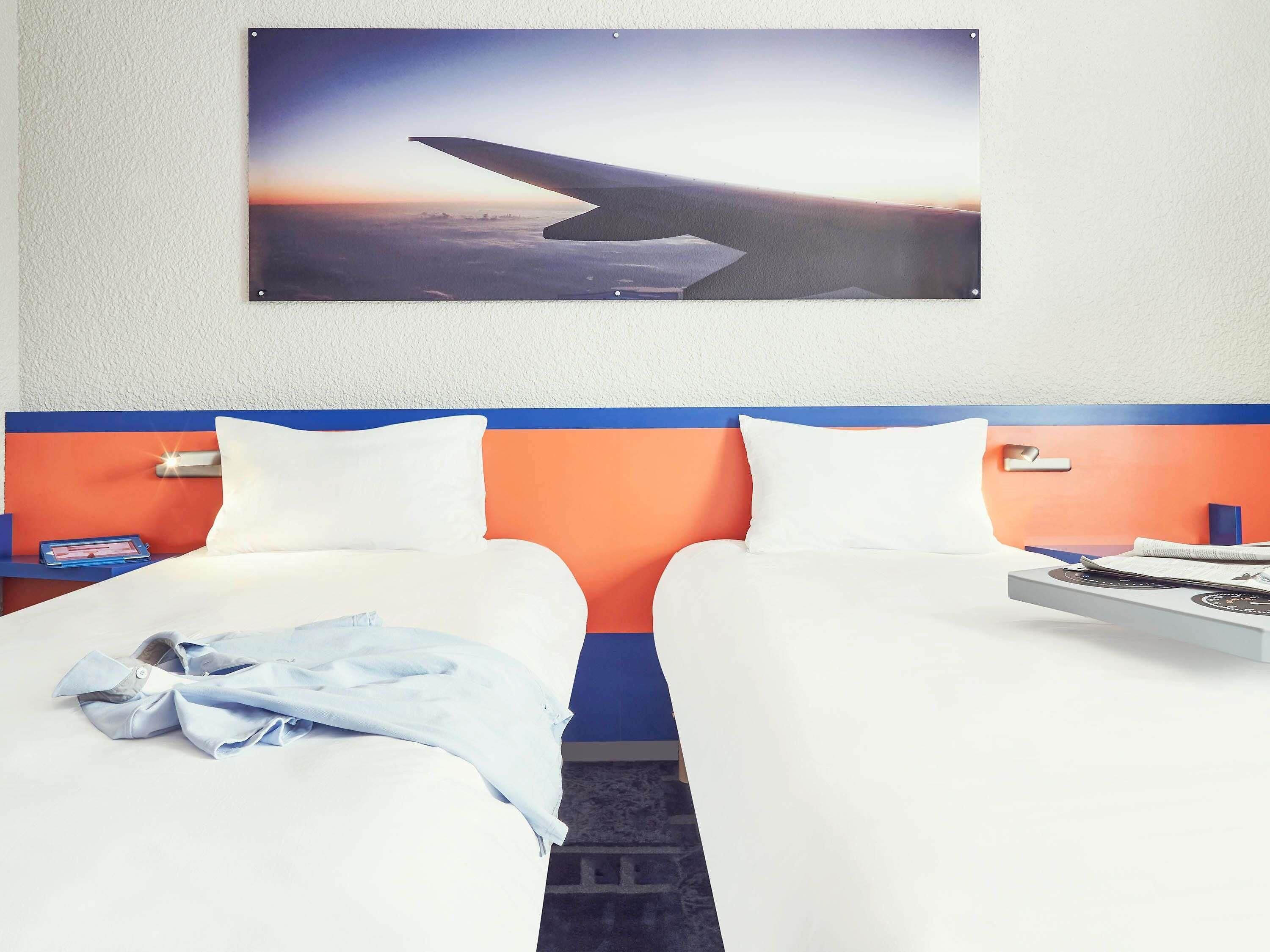 A hotel room with two beds, a large window with a view of an airplane wing, and a wall-mounted picture.