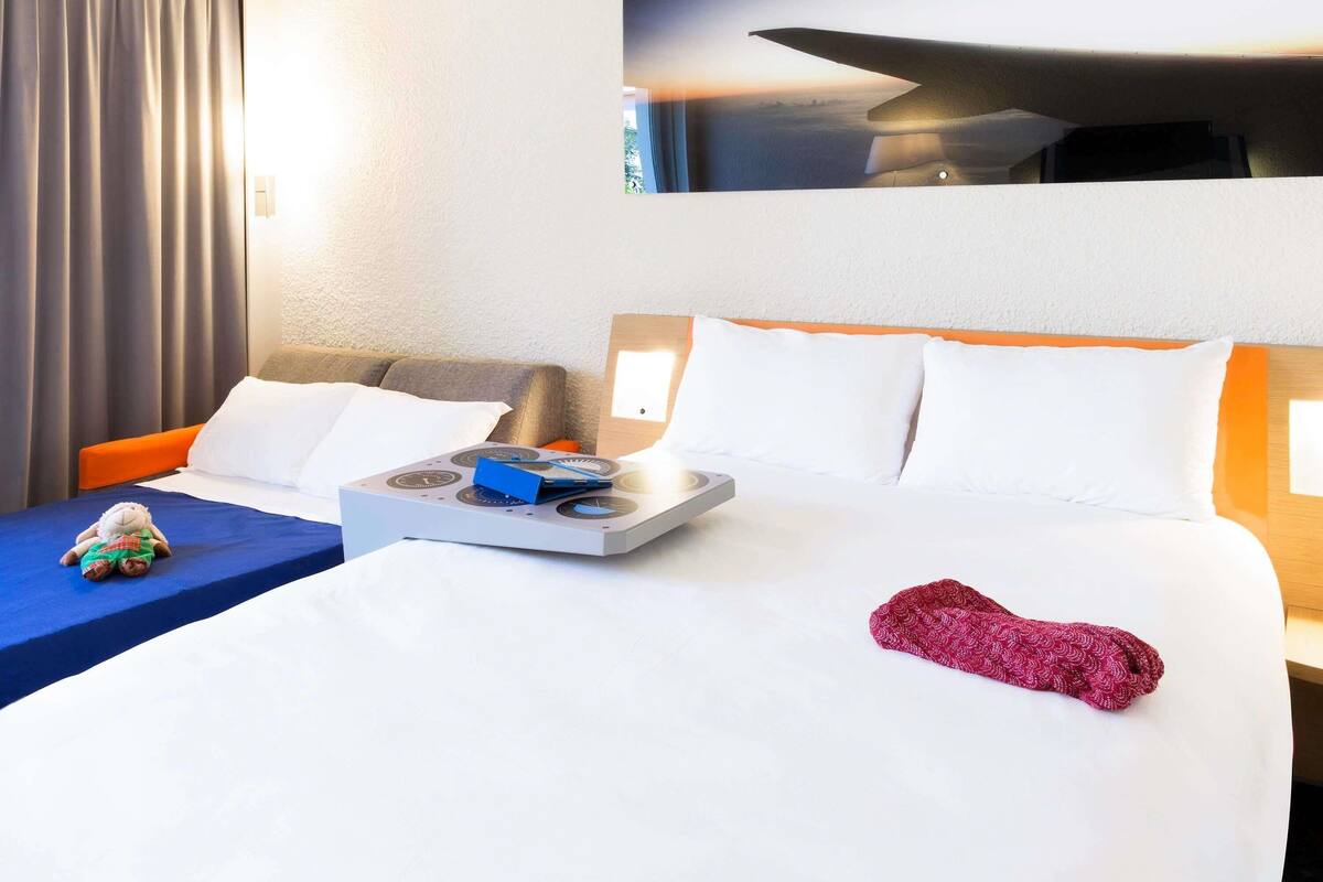 Een hotelkamer met een bed, een klein tafeltje met een dienblad, een stoel, een raam met uitzicht en een wandlamp.