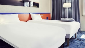 Habitación de hotel con dos camas, una ventana con cortinas, una lámpara y una obra de arte colgada en la pared.