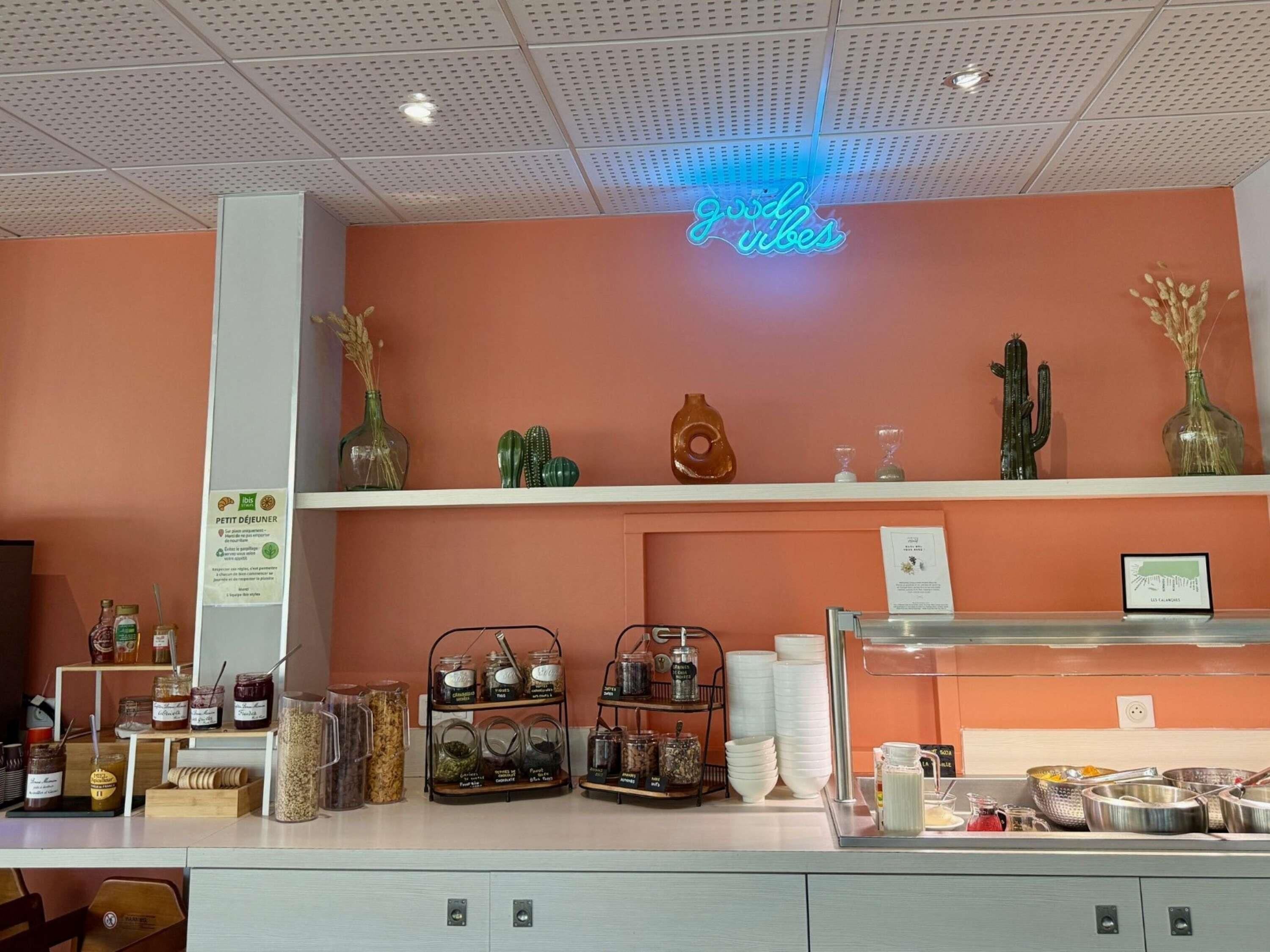 A cafe interior with a neon sign, shelves with jars and containers, and a counter with various items.
