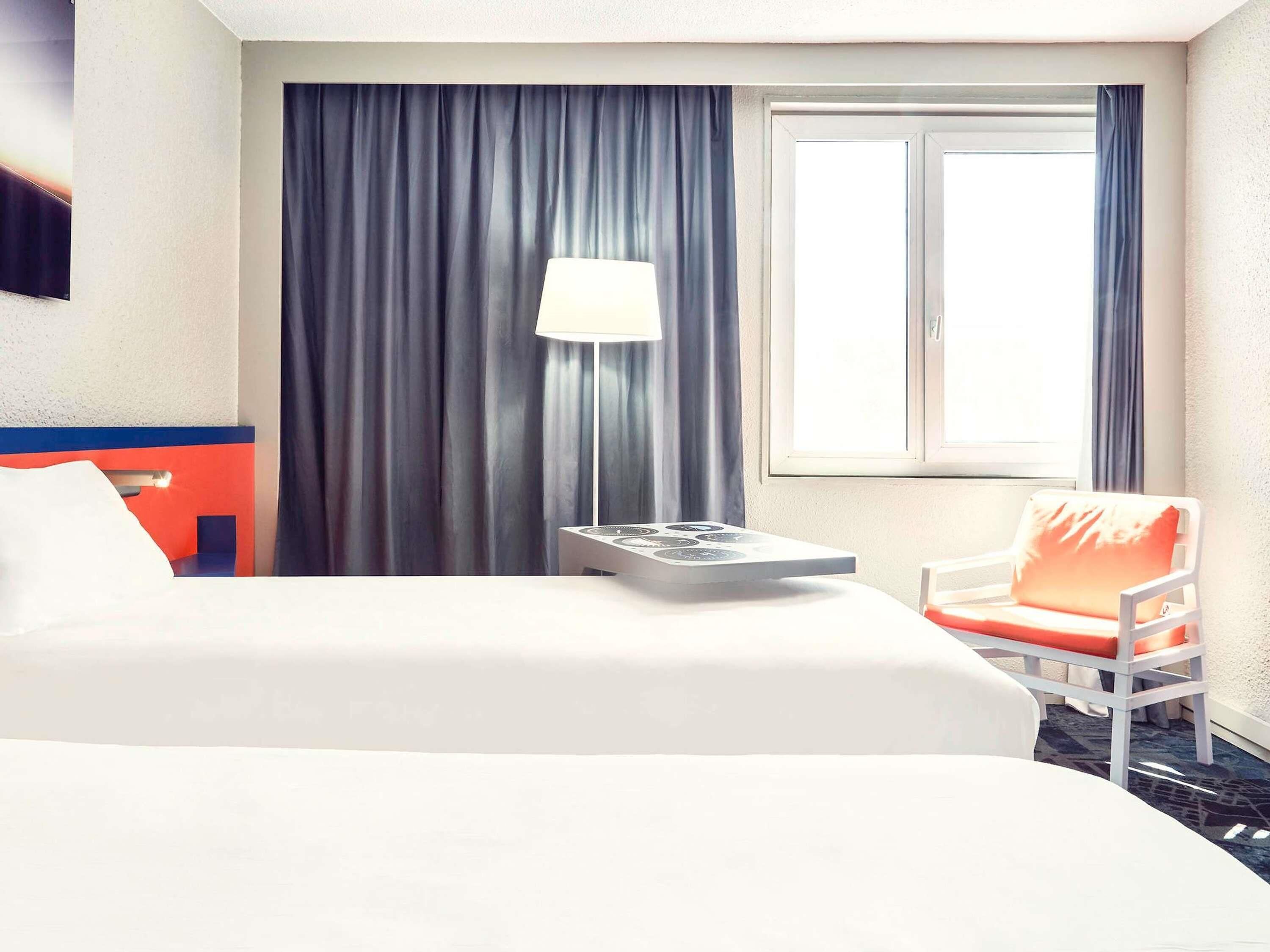 Una habitación de hotel con cama, una silla, una lámpara y un ventanal con cortinas.