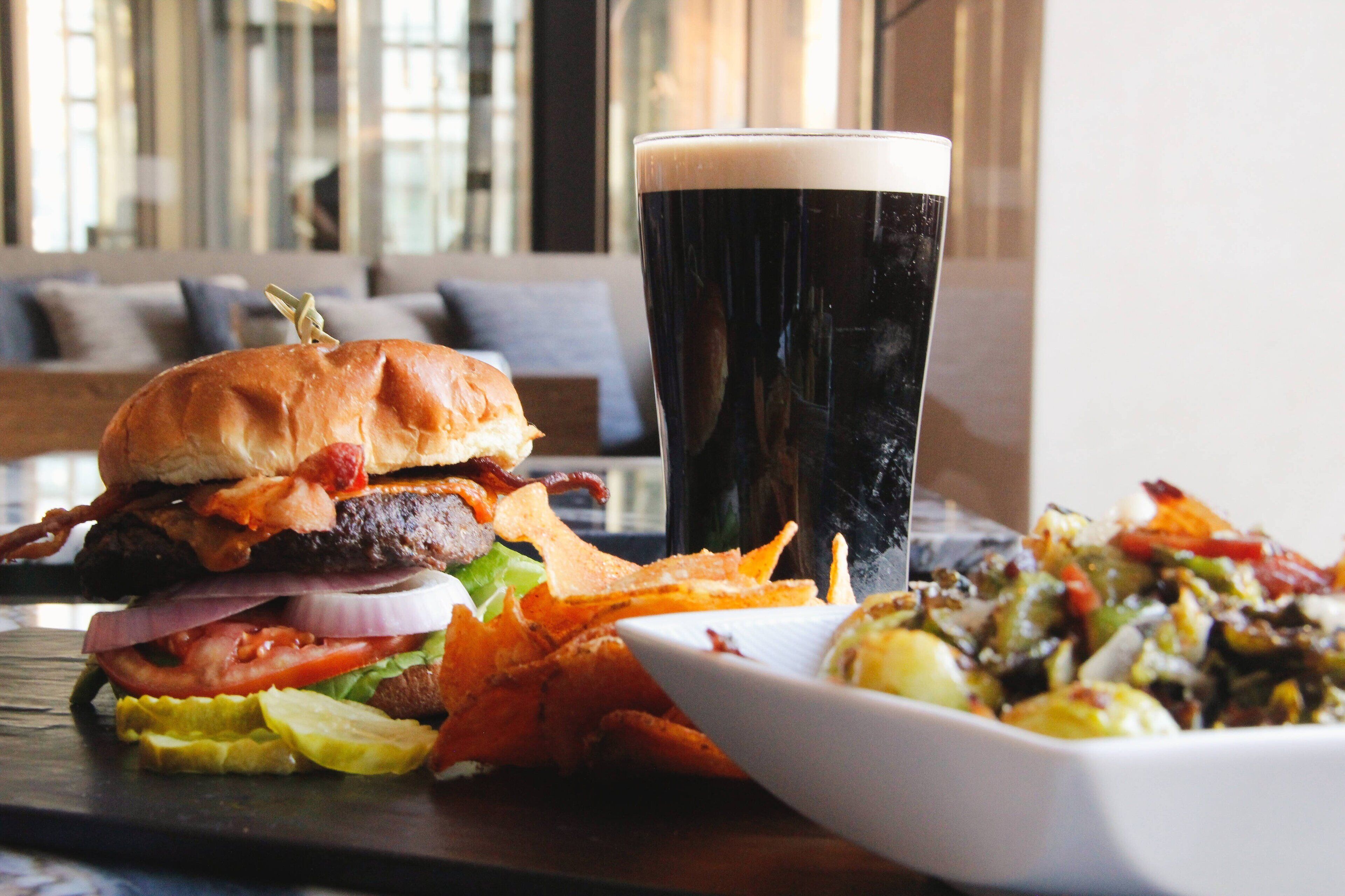 Ein Essen mit einem Burger, einem Glas dunklem Bier und einem kleinen Salat auf einem Tisch.
