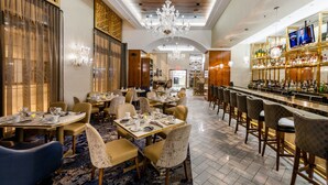 Un restaurante con mesas redondas, asientos de bar, candelabros y una zona de bar con botellas.