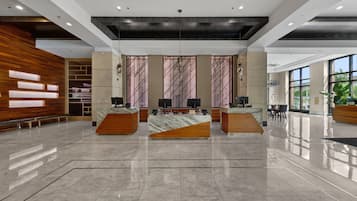 Welcome to our hotel lobby, featuring three reception desks, a polished floor, and a seating area with chairs and a table.