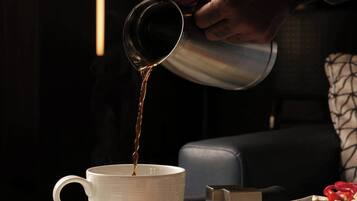 A person pouring a beverage into a cup, a plate with a dessert, and a small metal container on a table.