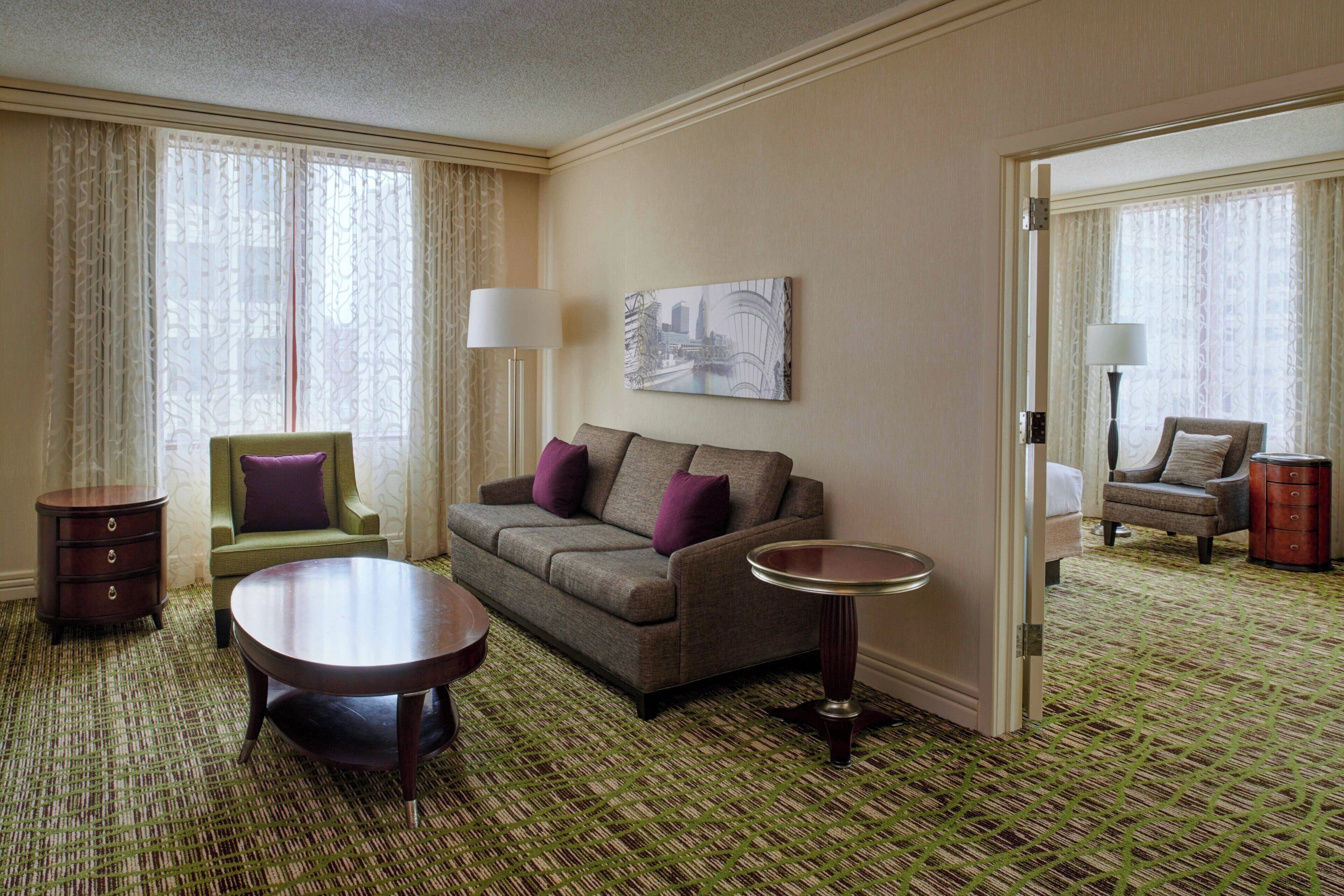 A hotel room with a sofa, armchair, side table, and a mirror.