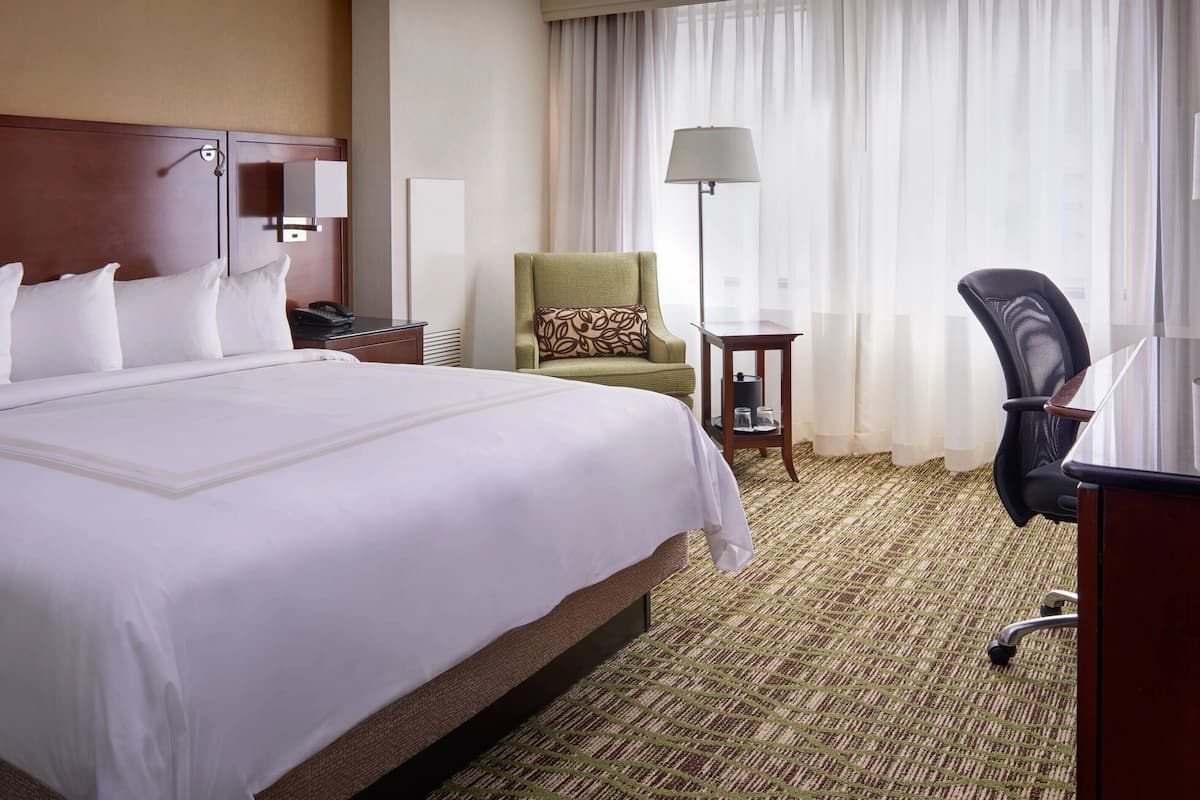 A hotel room with a large bed, a desk, a chair, a lamp, and a window with curtains.