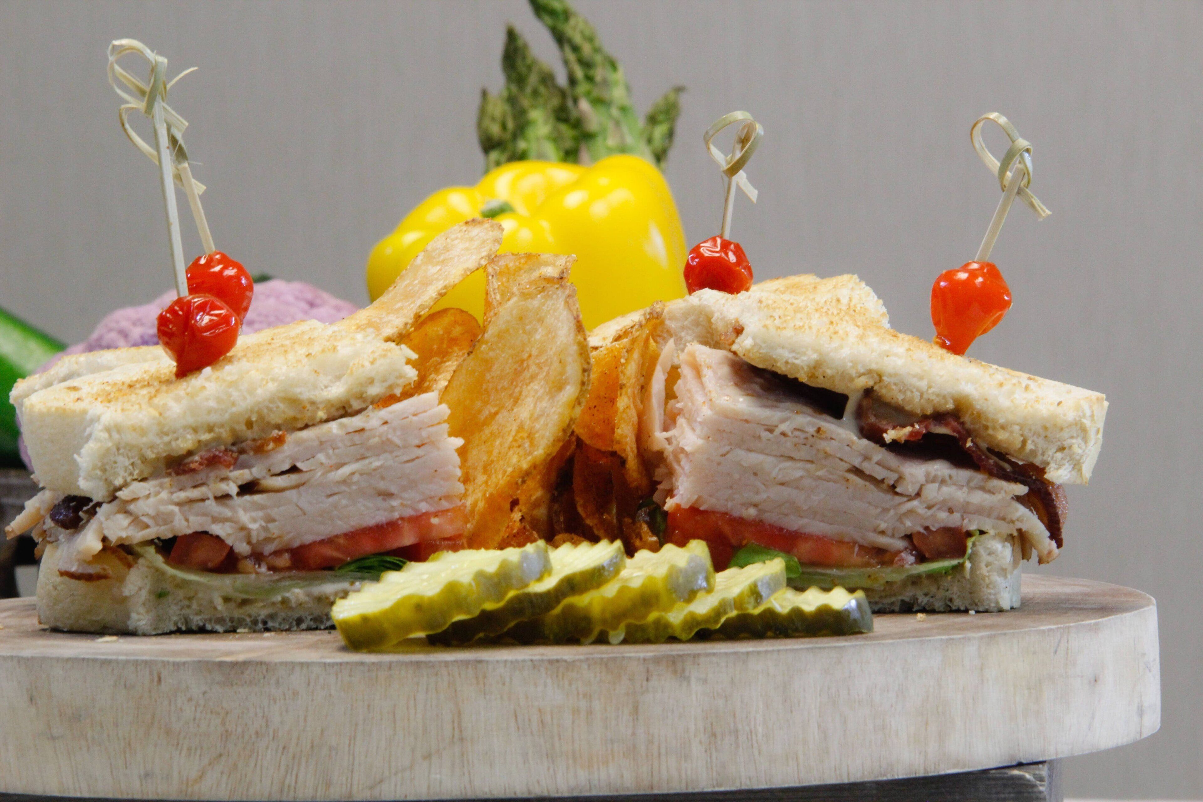 A sandwich with a toothpick garnish, surrounded by vegetables and pickles.