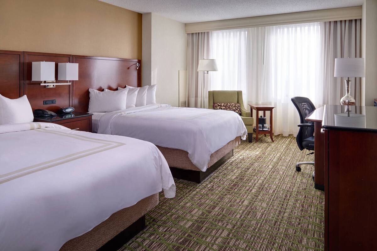 A hotel room with two beds, a desk, a chair, a lamp, and a telephone.