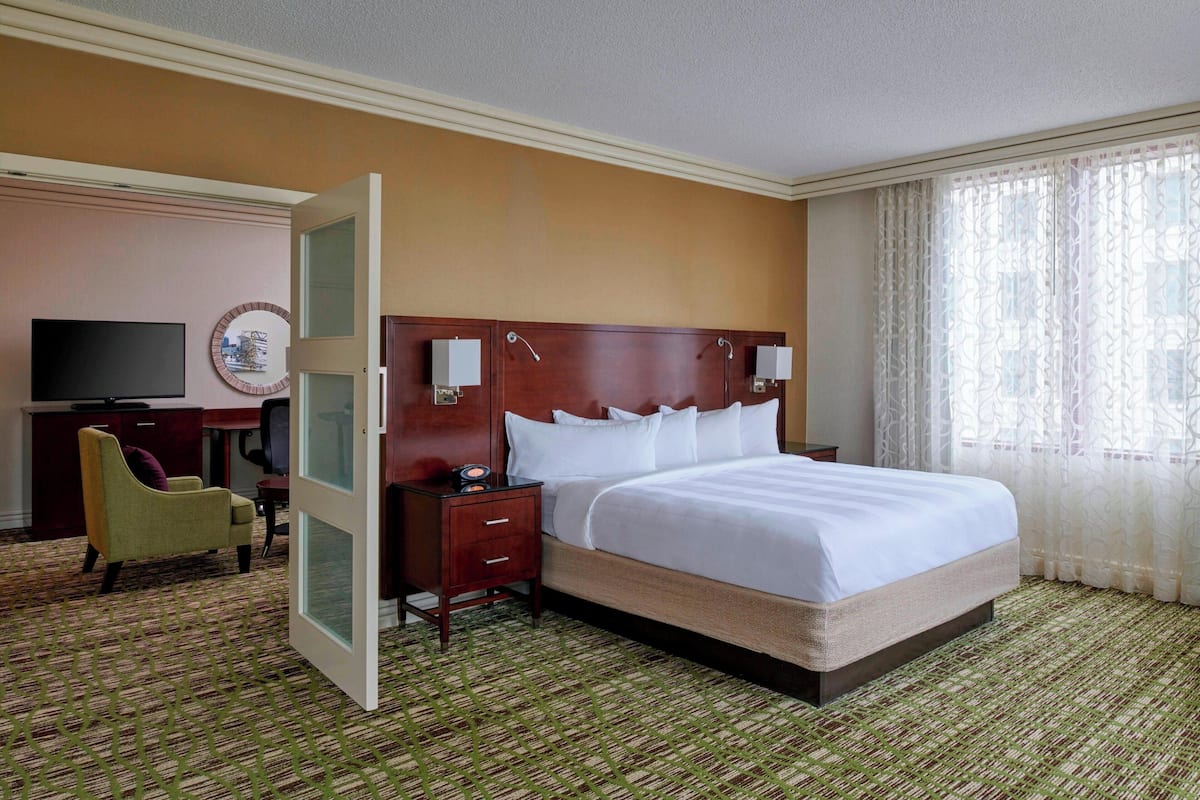 A hotel room with a large bed, a desk with a chair, a television, and a window with curtains.
