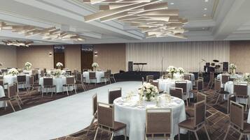 A banquet hall with round tables set for dining, a stage with musical instruments, and a carpeted floor.