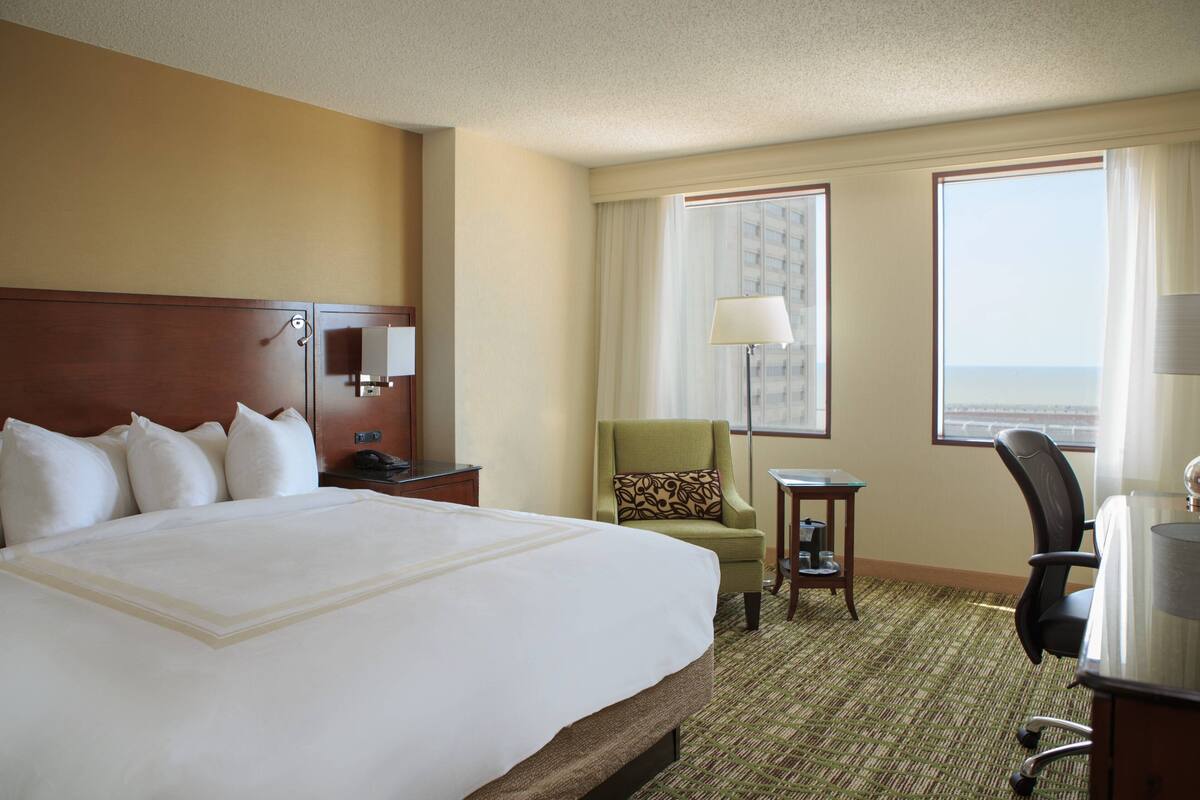A hotel room with a large bed, a desk, a chair, a small table, and a window with a view.