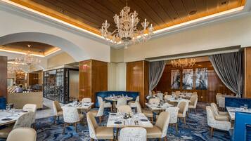 Une salle à manger d’hôtel avec plusieurs tables et chaises, un lustre et un meuble à vin en arrière-plan.
