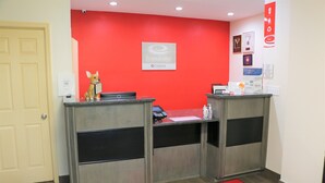 A reception area with a red wall, a receptionist desk, a small dog statue, and a welcome mat. - Econo Lodge Jasper (Jasper)