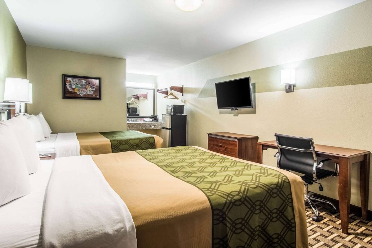 Habitación de hotel con dos camas, un escritorio, una silla, un televisor y una cafetera.