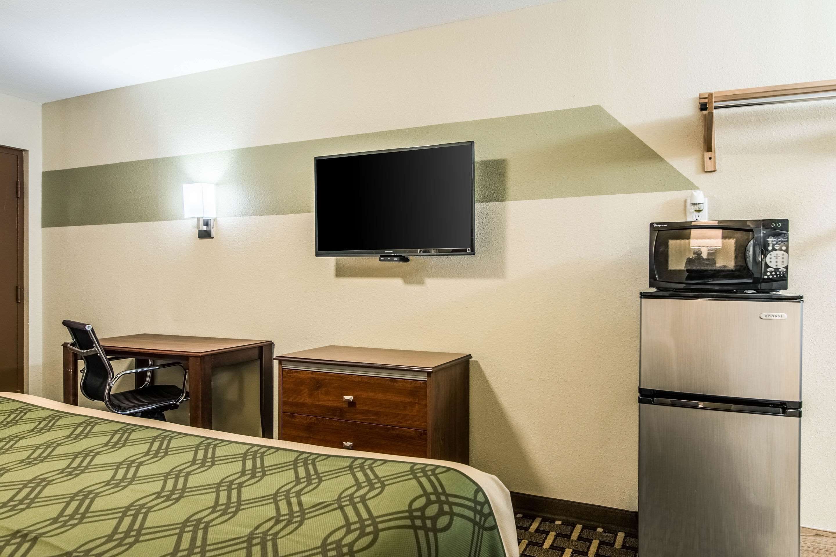 Una habitació d'hotel amb un llit, escriptori, cadira, televisió i nevera.