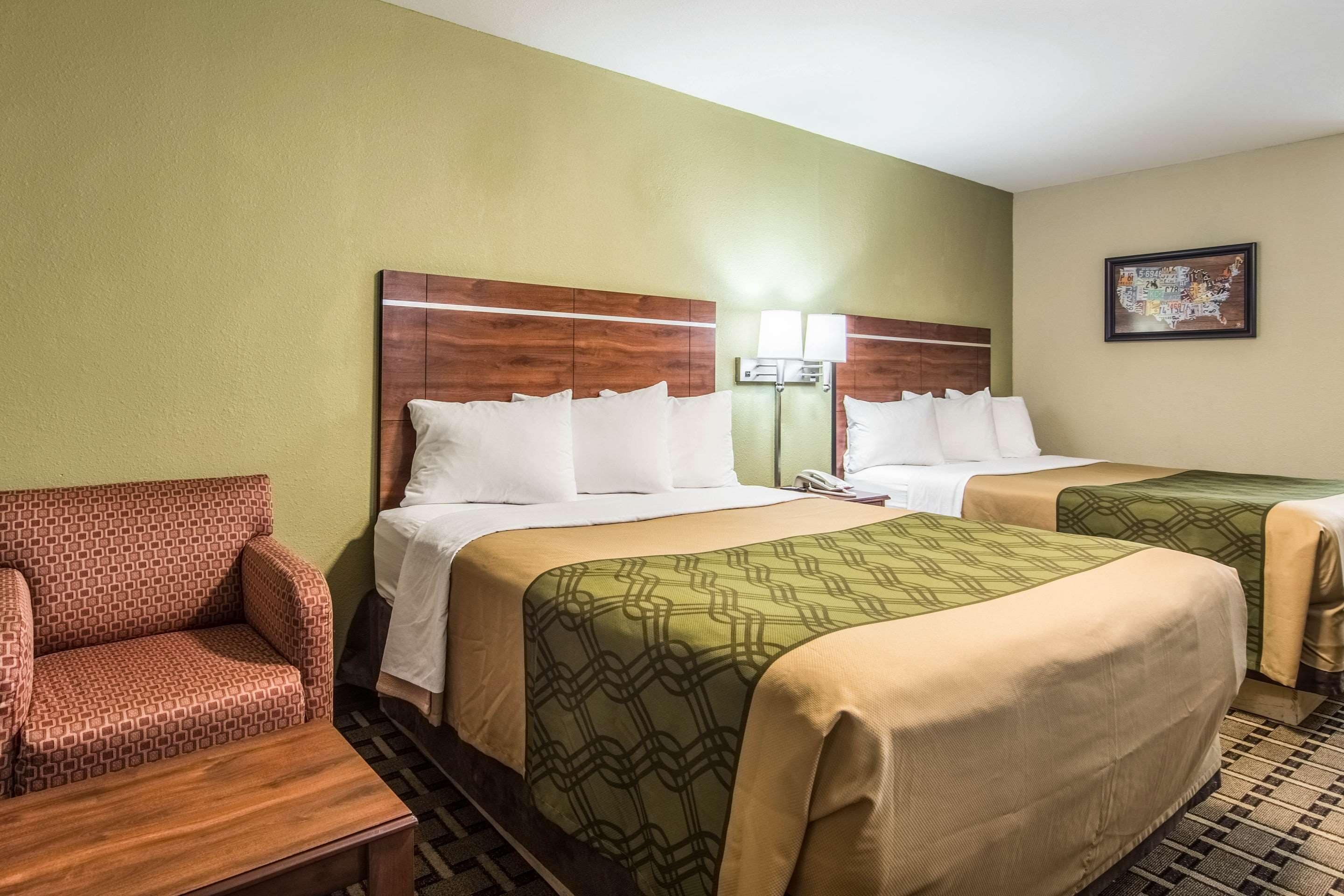 A hotel room with two beds, a sofa, a nightstand, and a wall-mounted lamp.