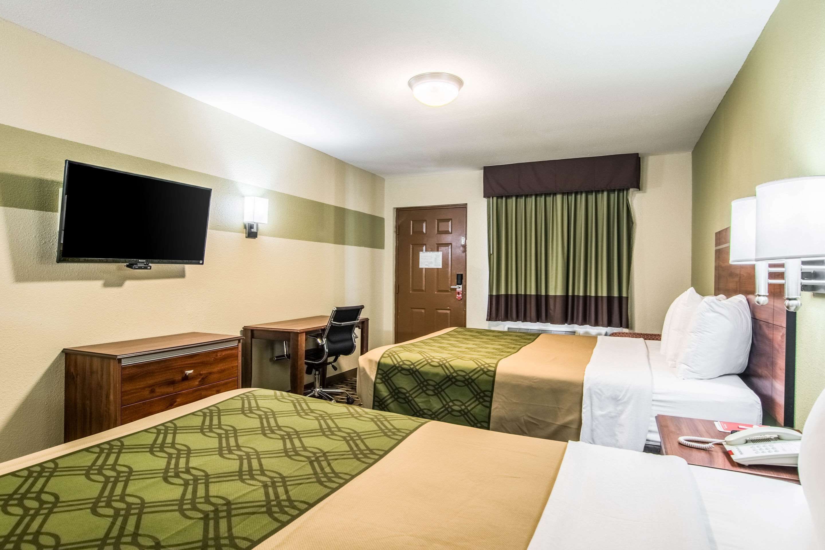 A hotel room with two beds, a desk, a chair, a television, a window with curtains, and a lamp.