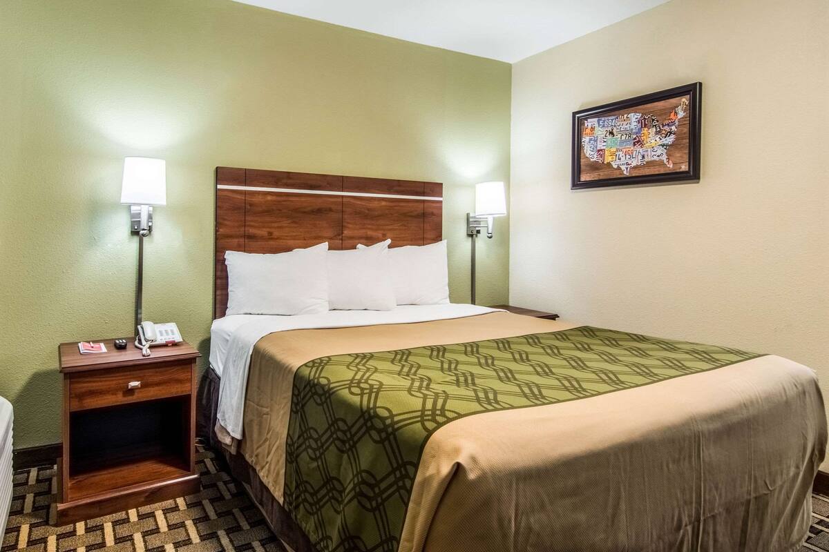 A hotel room with a wooden headboard, two bedside lamps, a phone on the nightstand, and a map artwork on the wall.