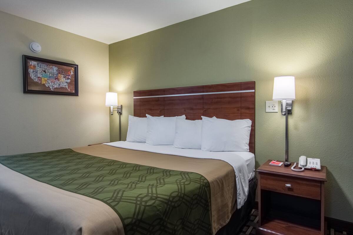 Una habitación de hotel con una cama grande, dos mesitas de noche con lámparas, un reloj de pared y un mapa enmarcado en la pared.