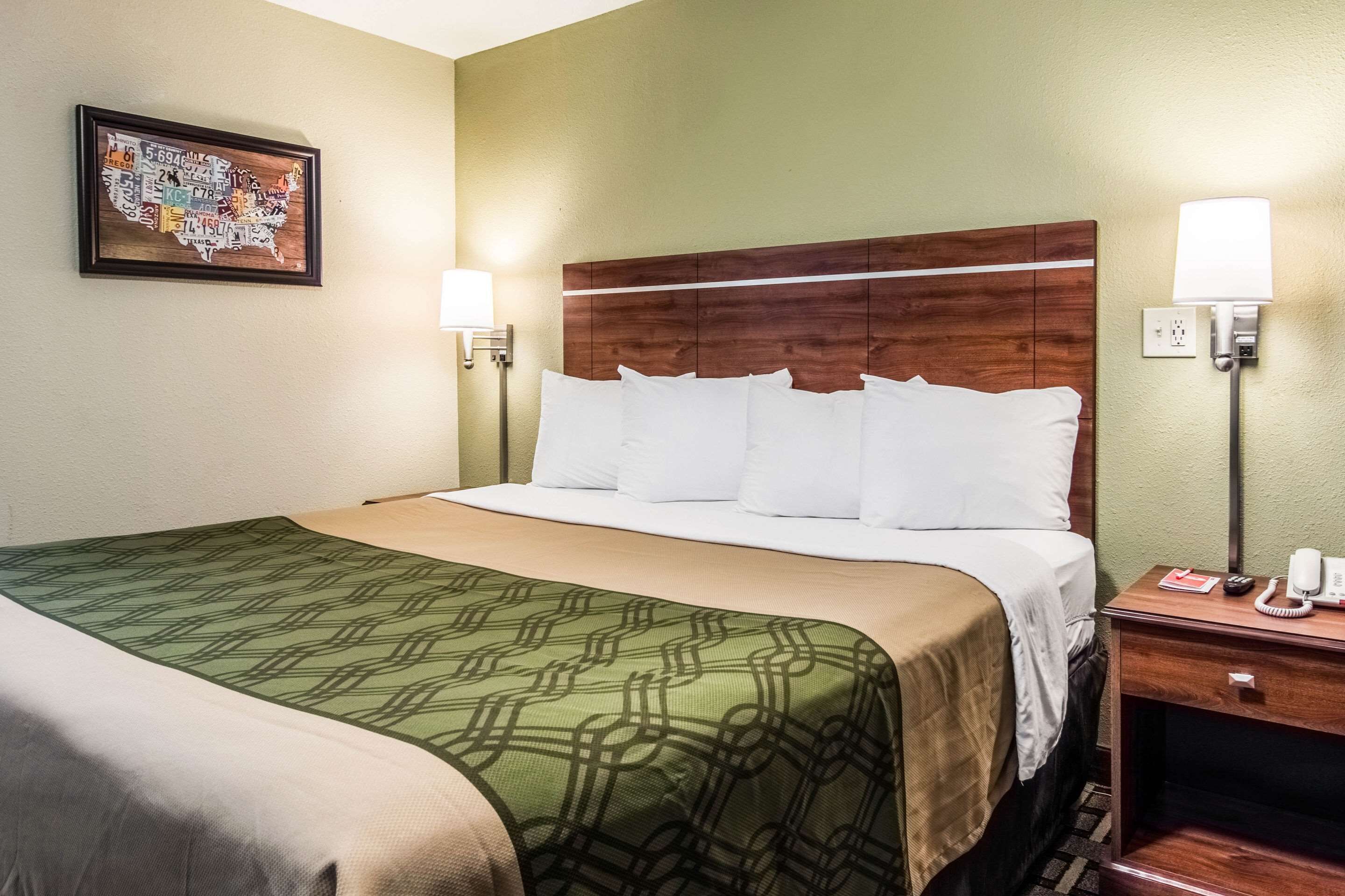 A hotel room with a bed, a nightstand, a lamp, and a framed map on the wall.