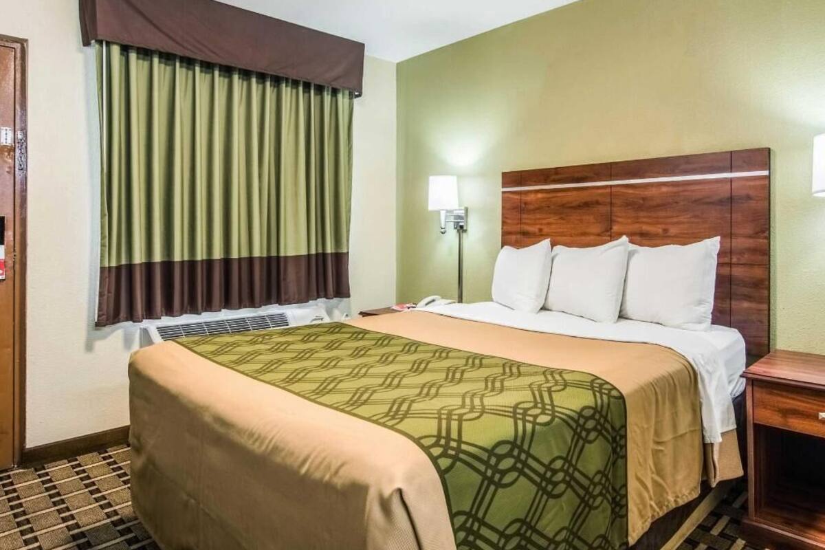 Quarto de hotel com cama, cortinas, mesa de cabeceira e abajur.