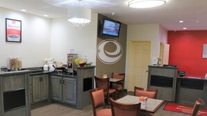 A hotel lobby with a kitchen area, dining tables, and chairs. There is a TV mounted on the wall and a door to the right. - Econo Lodge Jasper (Jasper)