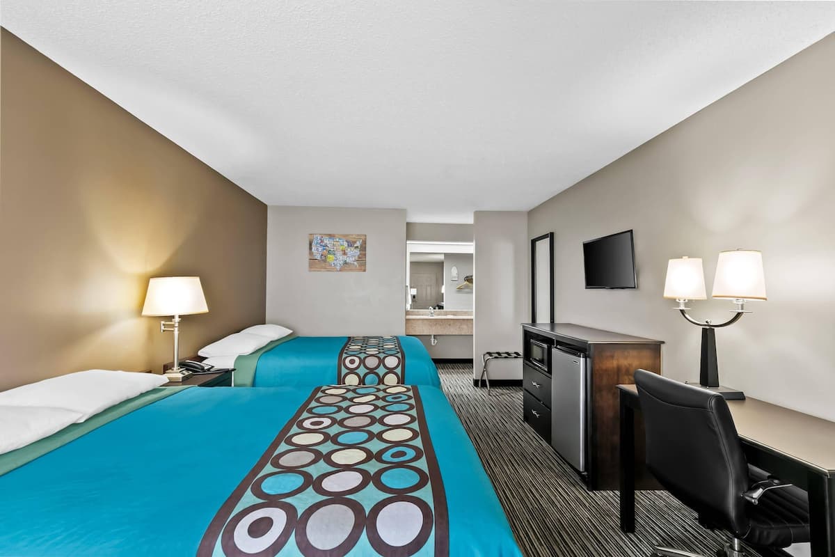 A hotel room with two beds, a desk, a chair, a TV, and a bathroom visible in the background.