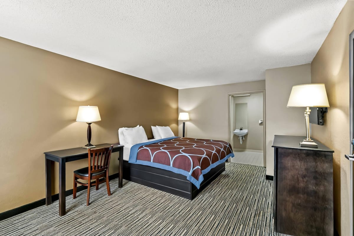 A hotel room with a bed, desk, chair, two lamps, and a small cabinet.