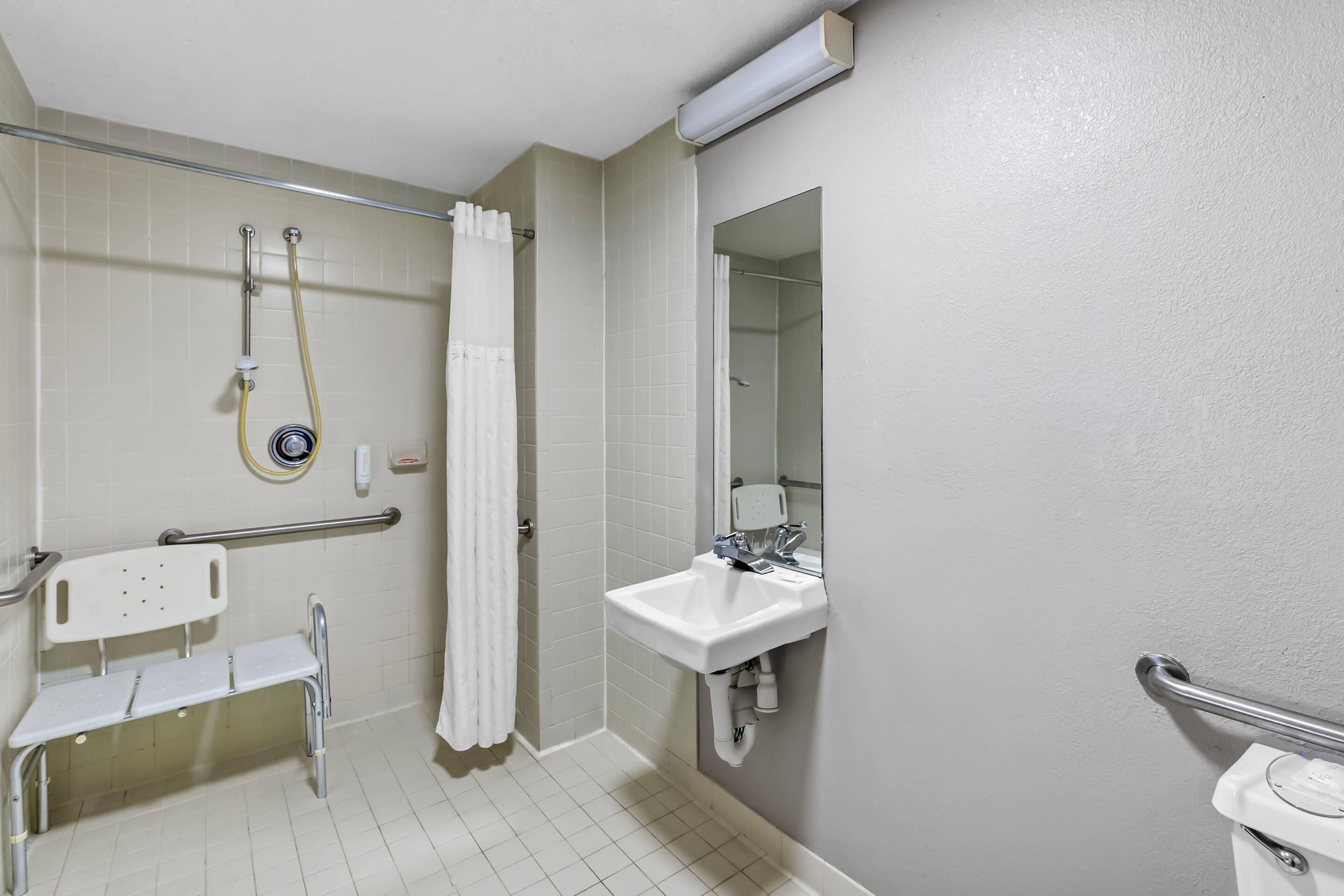 A bathroom with a shower, a sink, a toilet, and a bench.