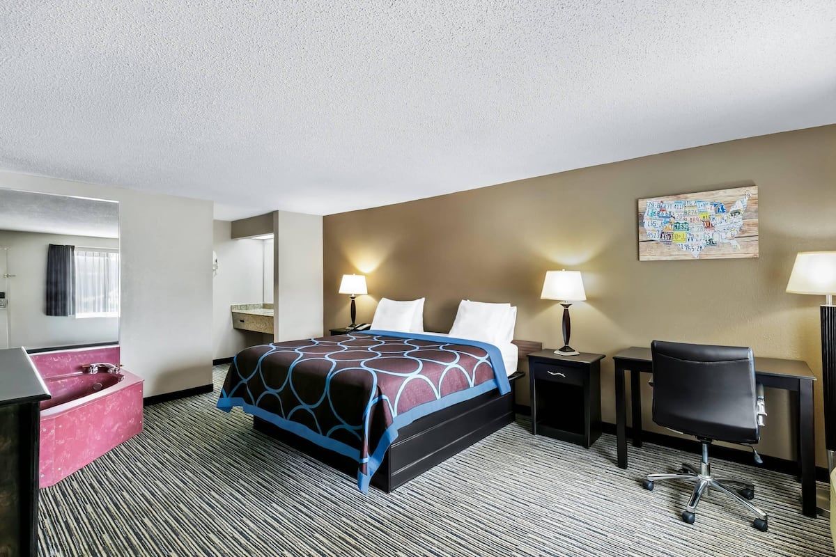 A hotel room with a bed, desk, chair, and a bathroom with a sink and mirror.