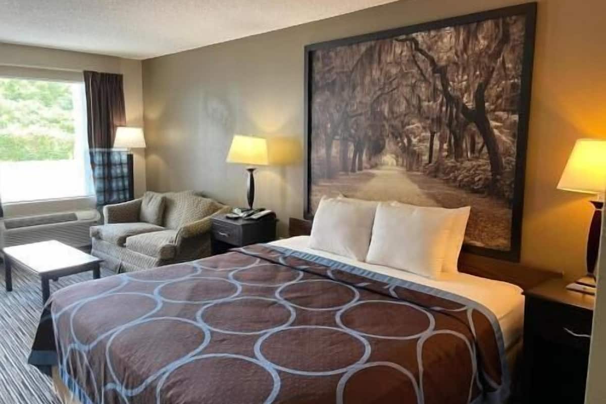 A hotel room with a bed, a chair, a desk, a lamp, and a large painting on the wall.