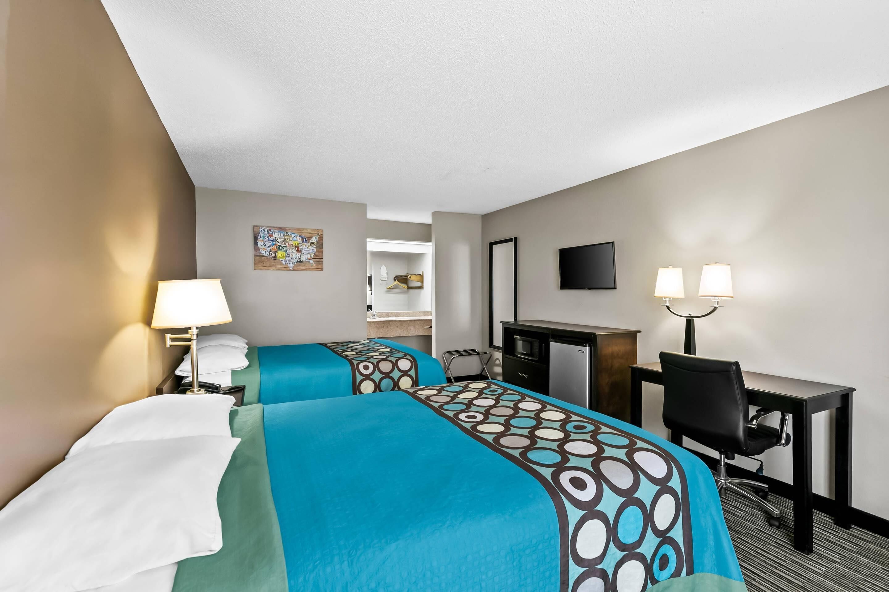 A hotel room with two beds, a desk, a chair, a TV, and a lamp.
