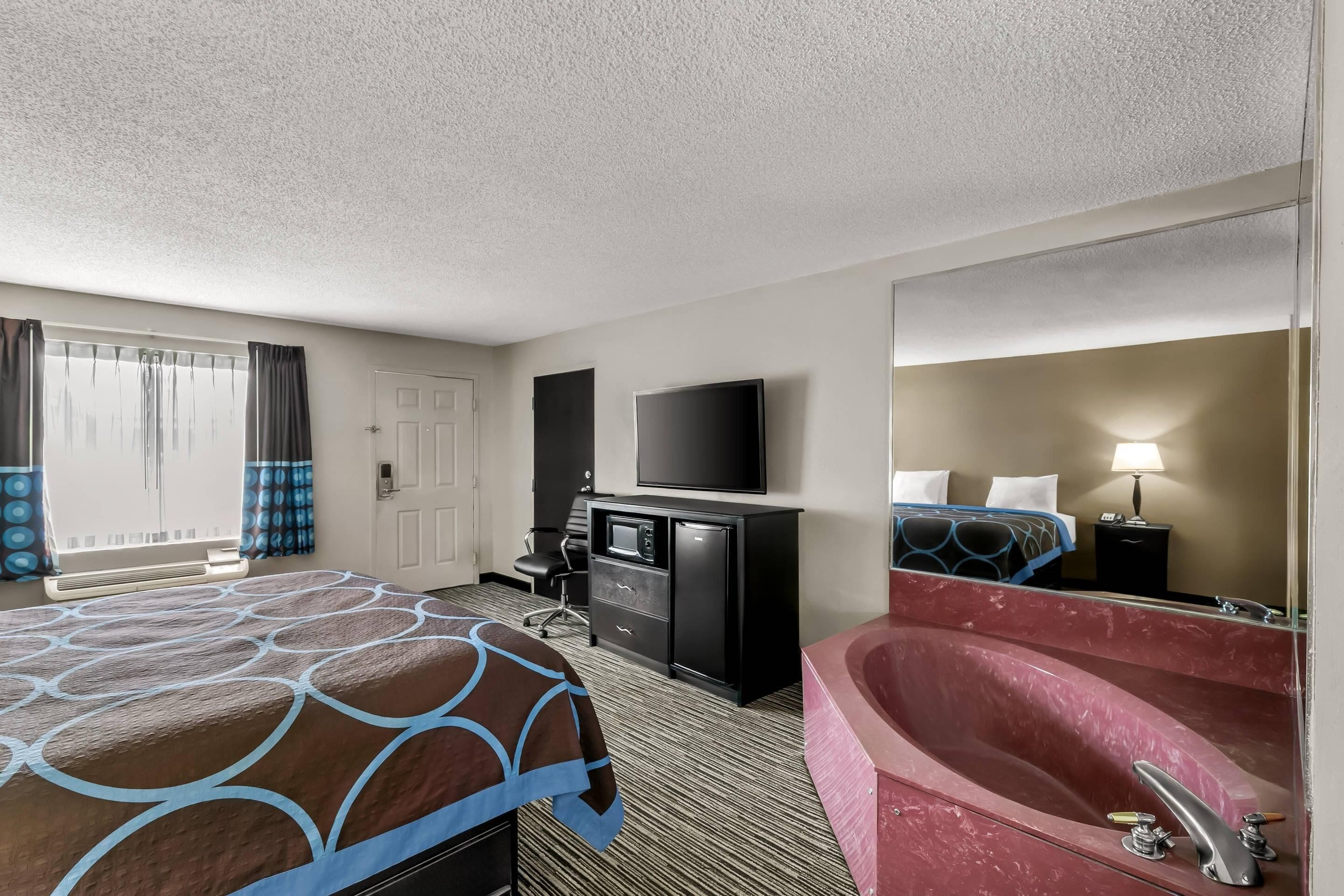 Een hotelkamer met een groot bed, een bureau met een flatscreen televisie, een zwarte dressoir, een grote spiegel en een rode whirlpool.