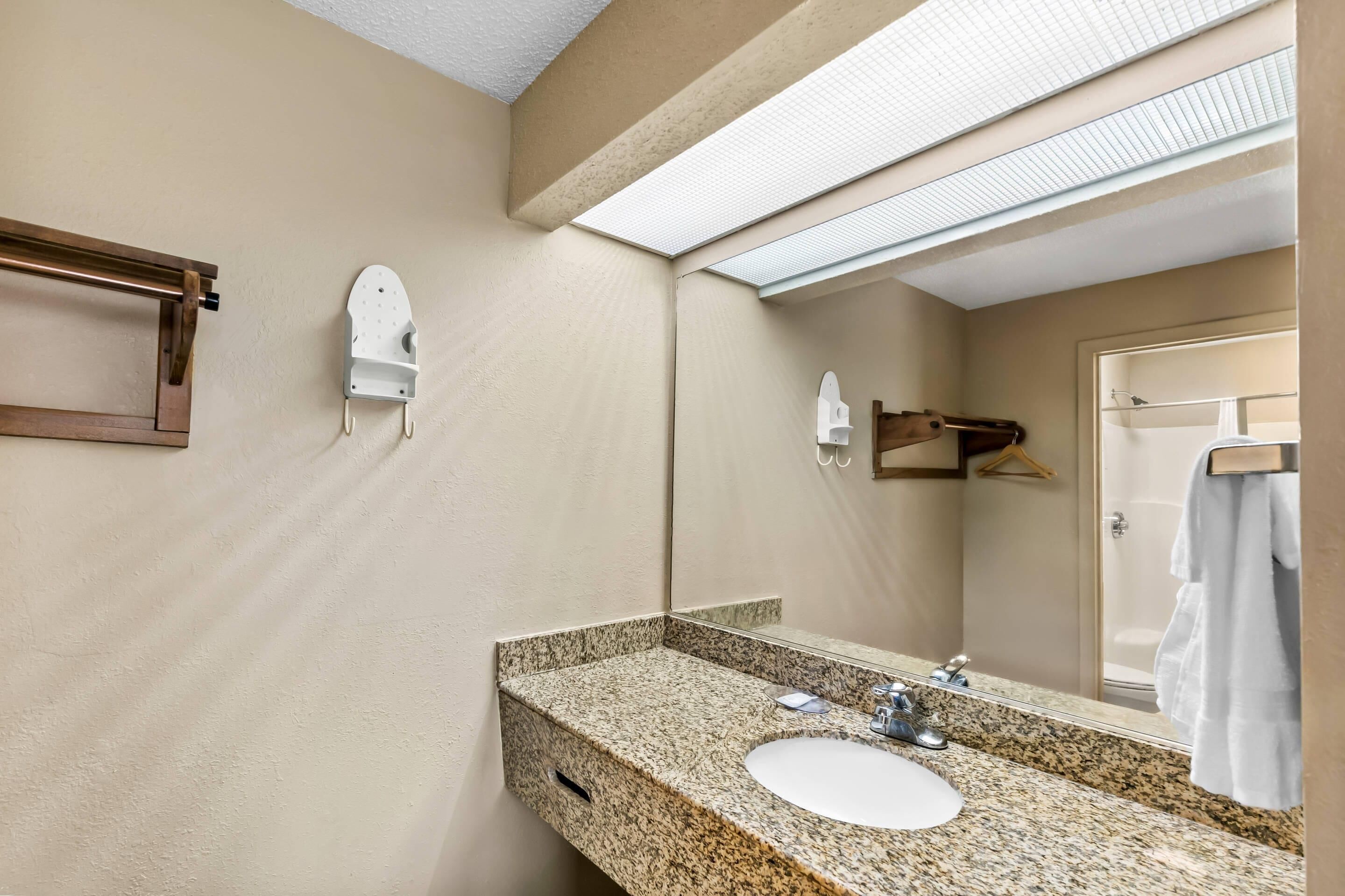 A bathroom with a granite countertop sink, a mirror, a towel rack, and a shower visible through the glass door.